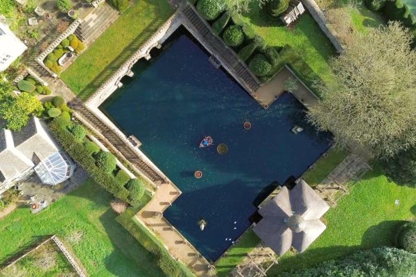 Aerial view of a large, irregularly shaped swimming pool with surrounding greenery and structures.
