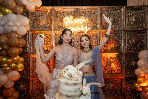 Two women celebrating at a wedding with a decorated cake.